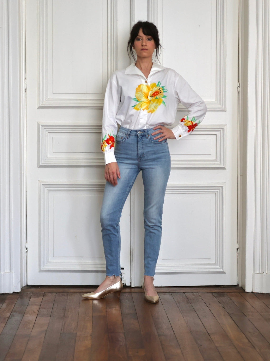 Chemise vintage Escada Margaretha Ley en coton blanc à imprimé hibiscus rouge et jaune, portée avec un jean clair, des escarpins dorés et un sac en macramé dans un look estival inspiré des vacances.